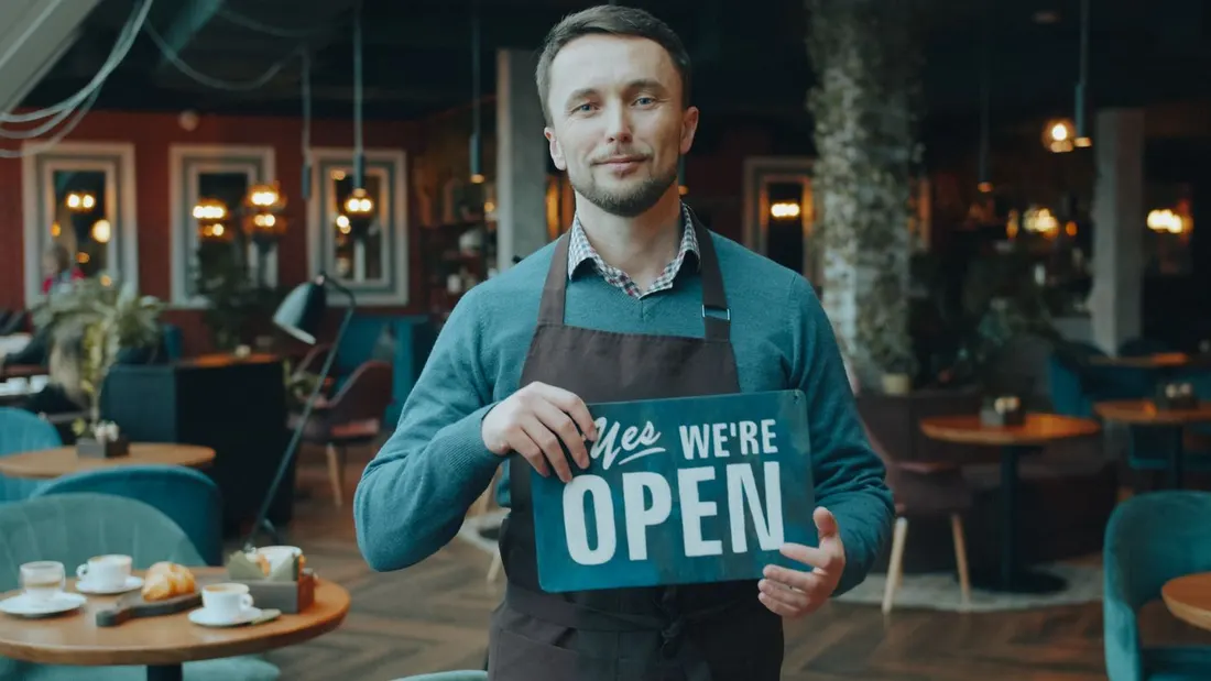 A café owner holding a sign that says we are open